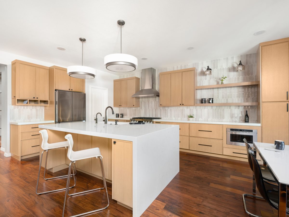 Open-concept kitchen with warm oak cabinetry, quartz island, and handmade-style picket tile backsplash — Reveal Interior Design Las Vegas