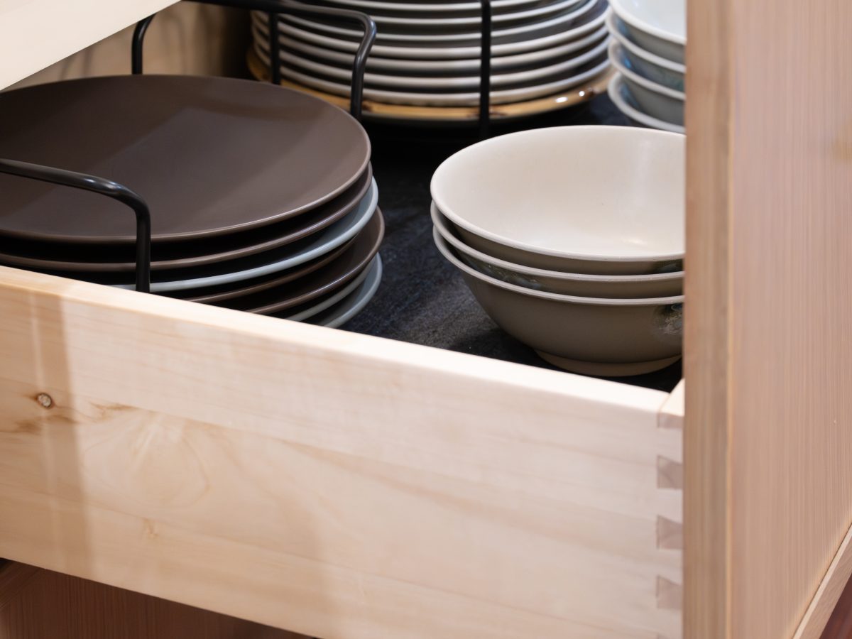 Kitchen pull-out drawer with organized dishware storage in warm oak cabinetry — Reveal Interior Design Las Vegas