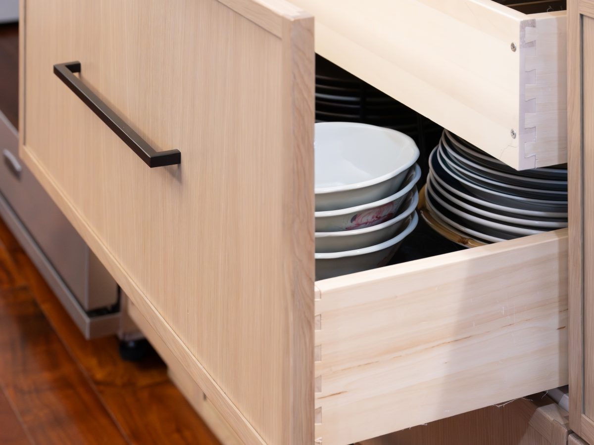 Kitchen island pull-out drawer storage with warm stained oak cabinetry and dark bronze hardware — Reveal Interior Design Las Vegas