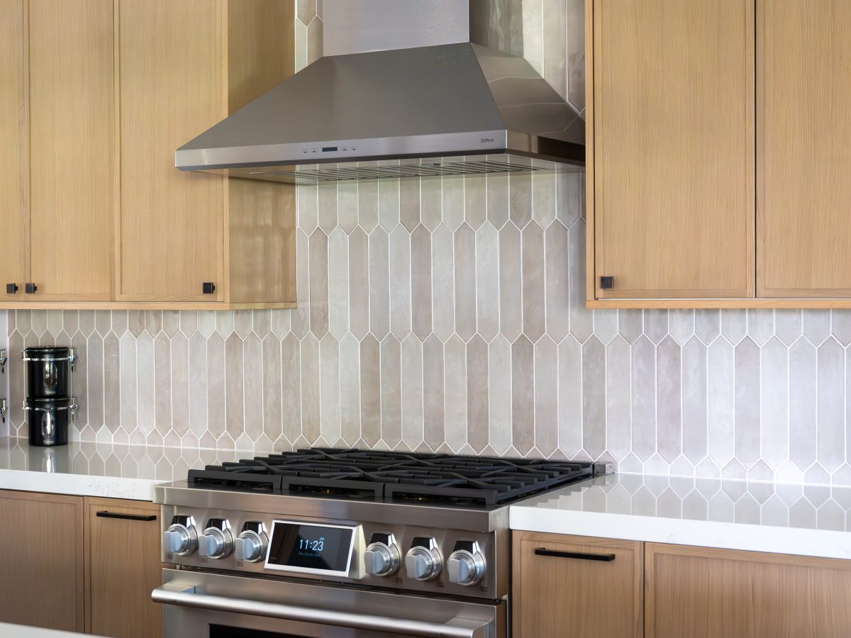 Kitchen with warm stained oak slim shaker cabinetry, picket backsplash tile, and quartz countertops — Reveal Interior Design Las Vegas