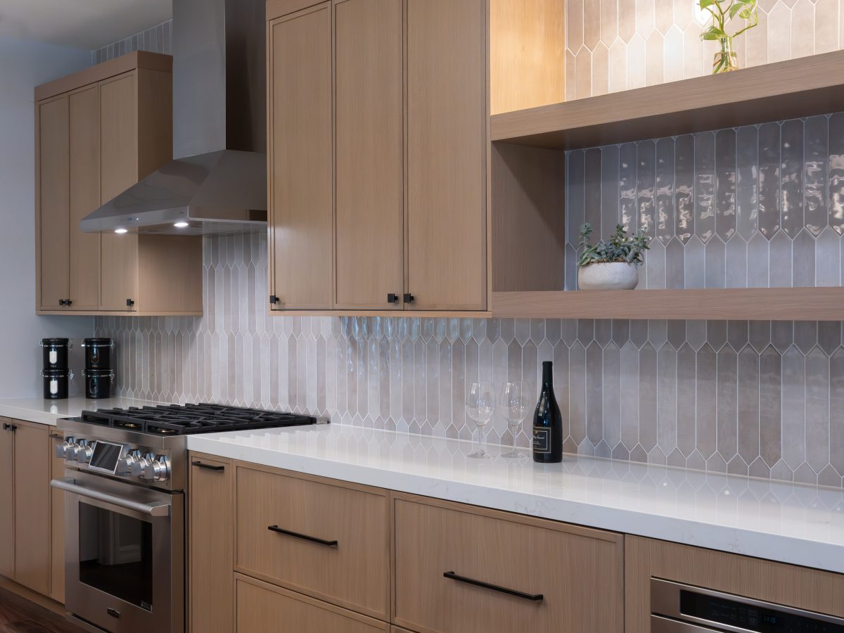 Modern kitchen with warm stained oak cabinetry, dark bronze hardware, and handmade-look picket backsplash tile — Reveal Interior Design Las Vegas