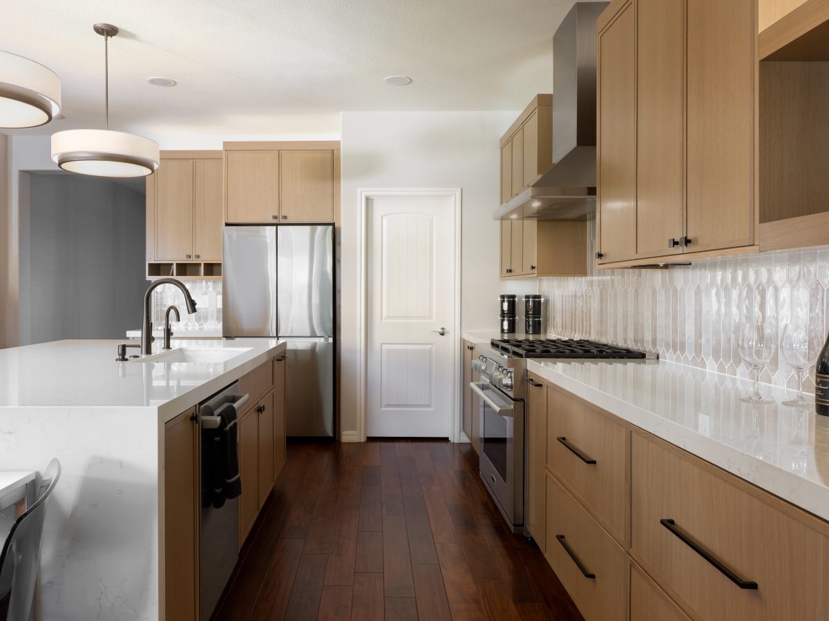 Warm oak shaker kitchen with quartz countertops and picket-shaped backsplash tile — Reveal Interior Design Las Vegas