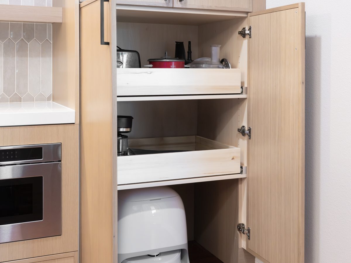 Kitchen appliance cabinet with pull-out shelves and built-in robot vacuum storage — Reveal Interior Design Las Vegas