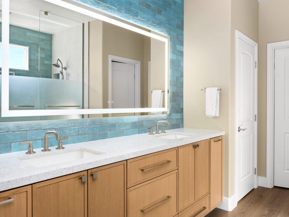 Primary bathroom double vanity with white quartz countertops, warm oak cabinetry, and handmade teal subway tile — Reveal Interior Design Las Vegas