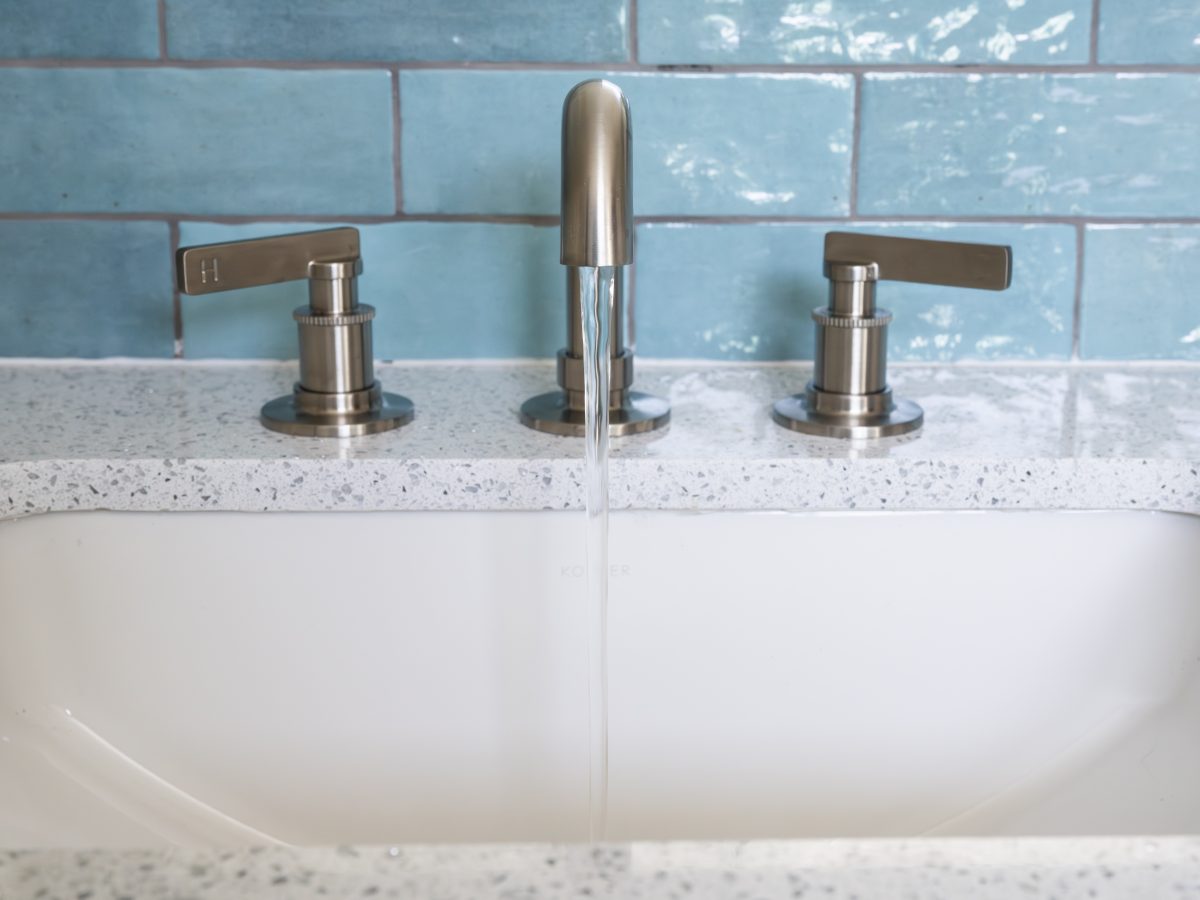 Primary bathroom vanity with white quartz countertop, brushed nickel fixtures, and handmade teal subway tile — Reveal Interior Design Las Vegas