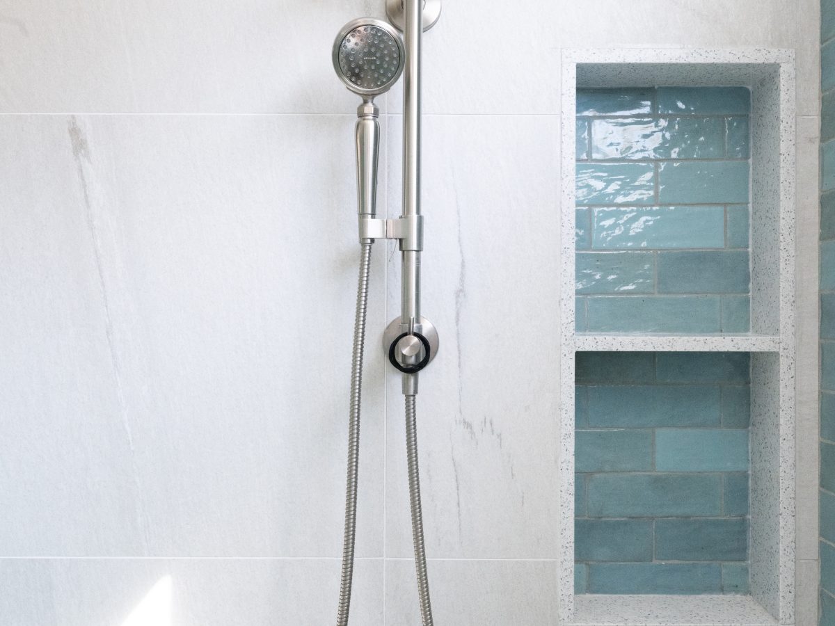 Primary bathroom shower with brushed nickel rain head, handshower, and teal handmade subway tile shampoo niches — Reveal Interior Design Las Vegas