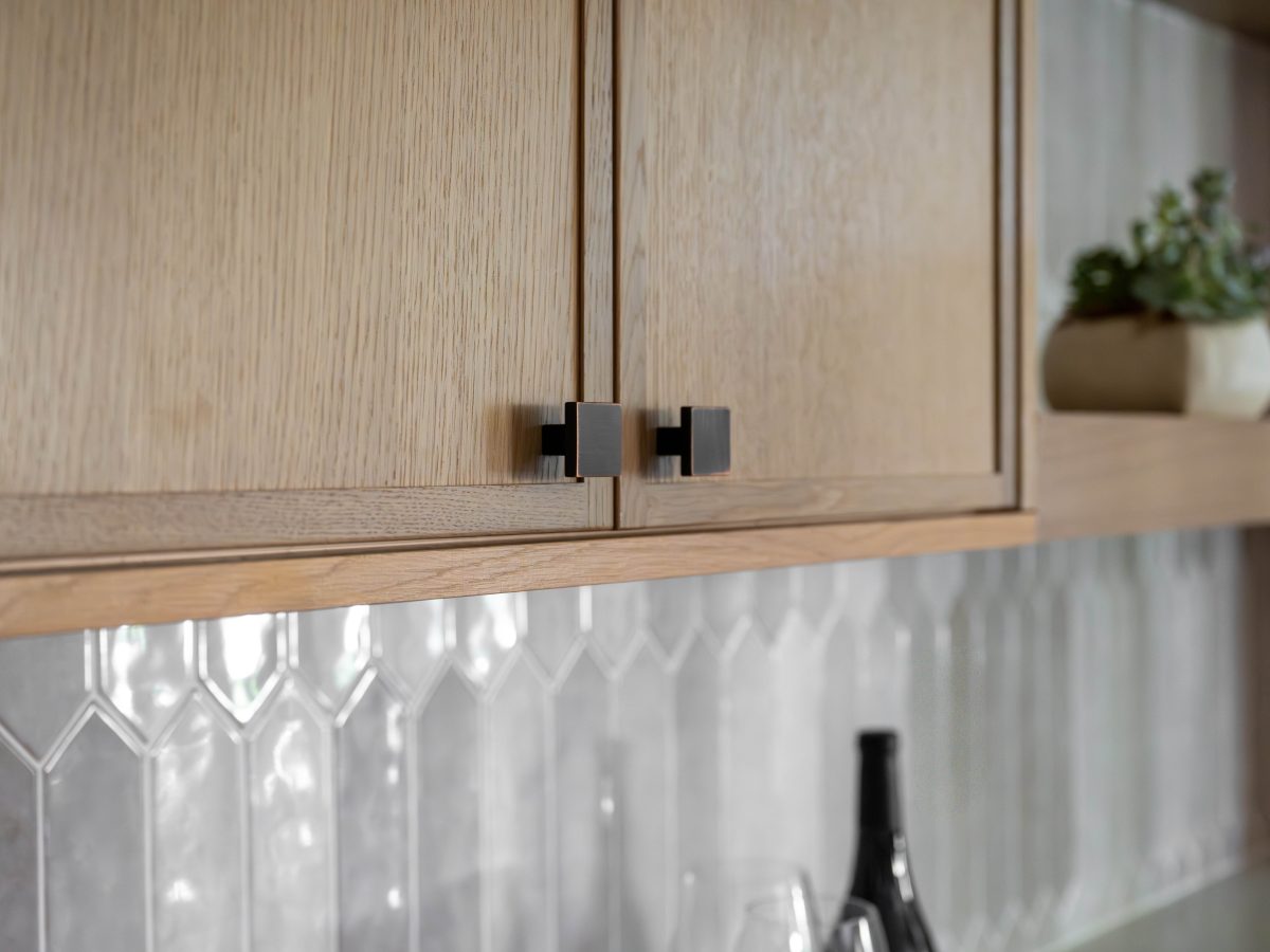 Kitchen upper oak shaker cabinets with dark bronze hardware and handmade-style picket backsplash tile — Reveal Interior Design Las Vegas