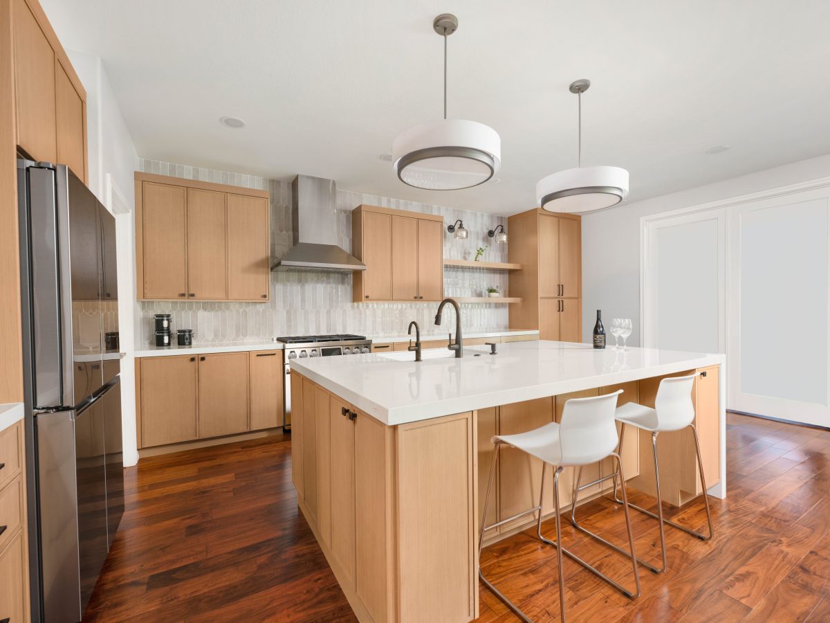 Modern kitchen with warm oak shaker cabinetry, quartz island, and dark bronze fixtures — Reveal Interior Design Las Vegas