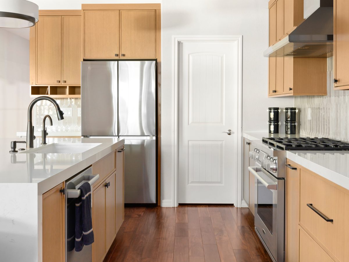 Galley kitchen with warm oak shaker cabinetry, quartz countertops, and stainless appliances — Reveal Interior Design Las Vegas