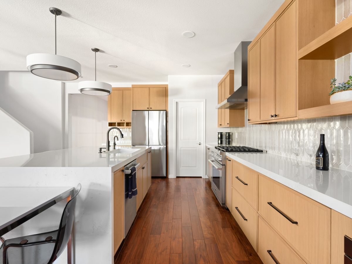 Galley kitchen with warm oak shaker cabinetry, quartz countertops, and picket backsplash tile — Reveal Interior Design Las Vegas