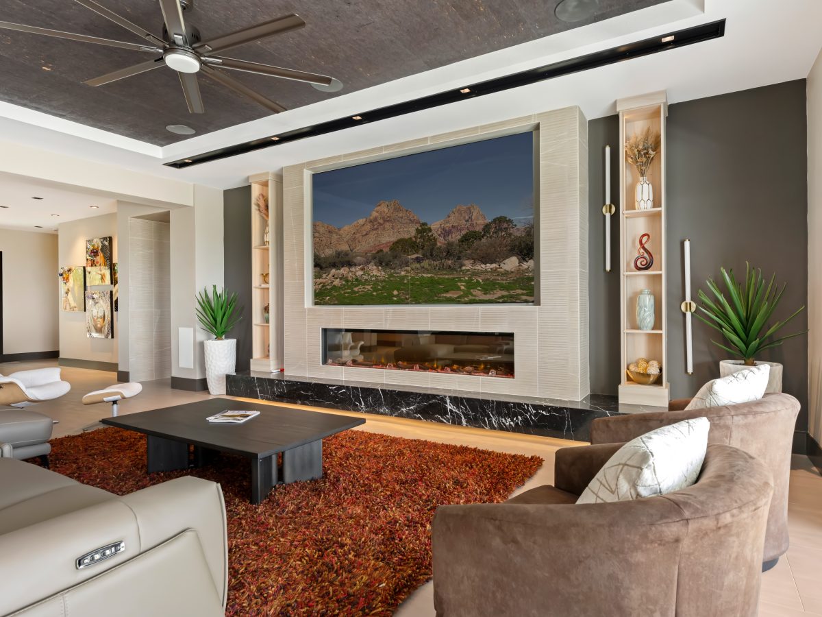 Living room with custom light wood bookcase cabinetry, linear fireplace, and four-panel TV wall — Reveal Interior Design Las Vegas