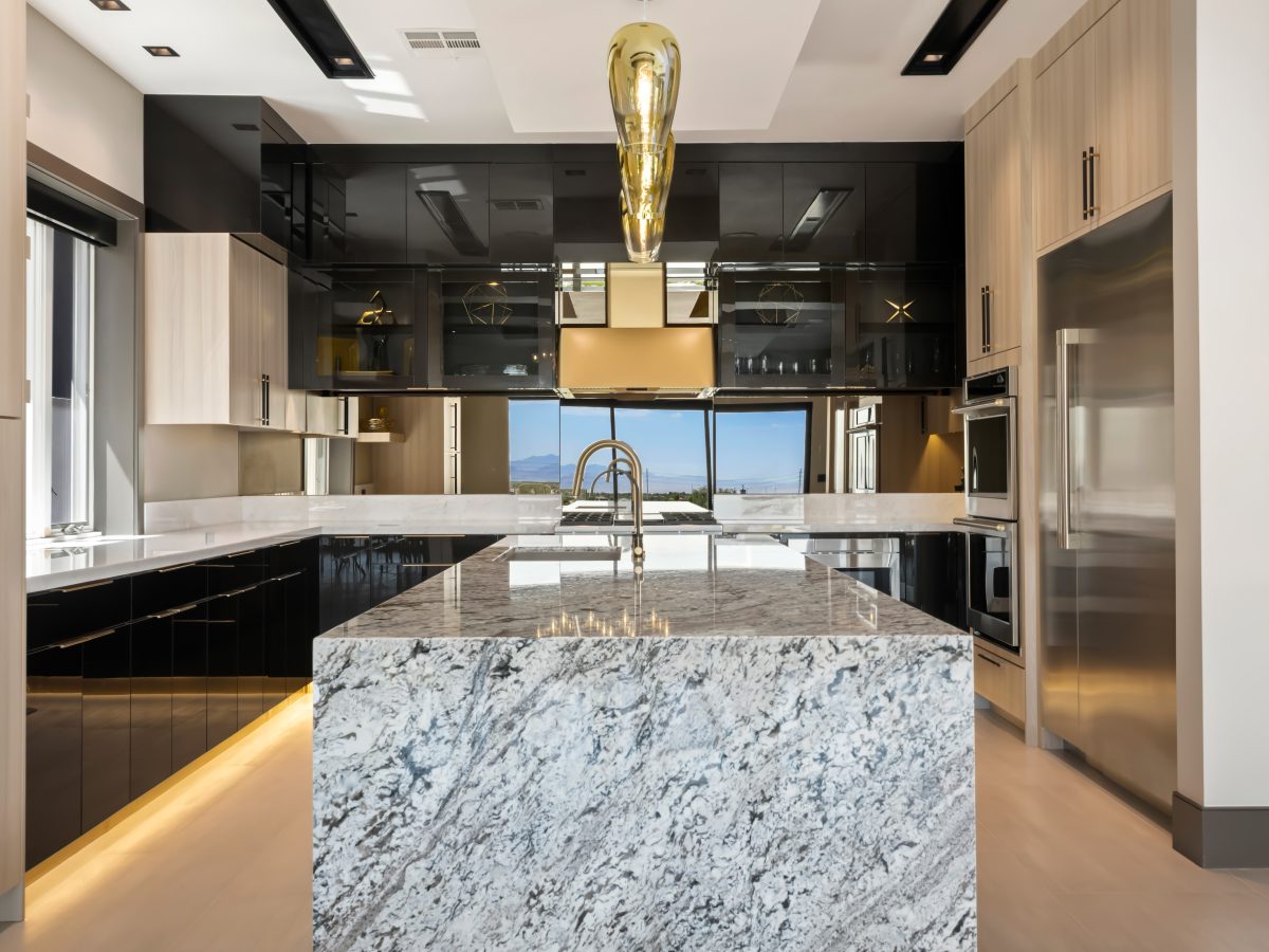 Luxury kitchen with granite waterfall island, charcoal gloss cabinetry, and gold accents — Reveal Interior Design Las Vegas