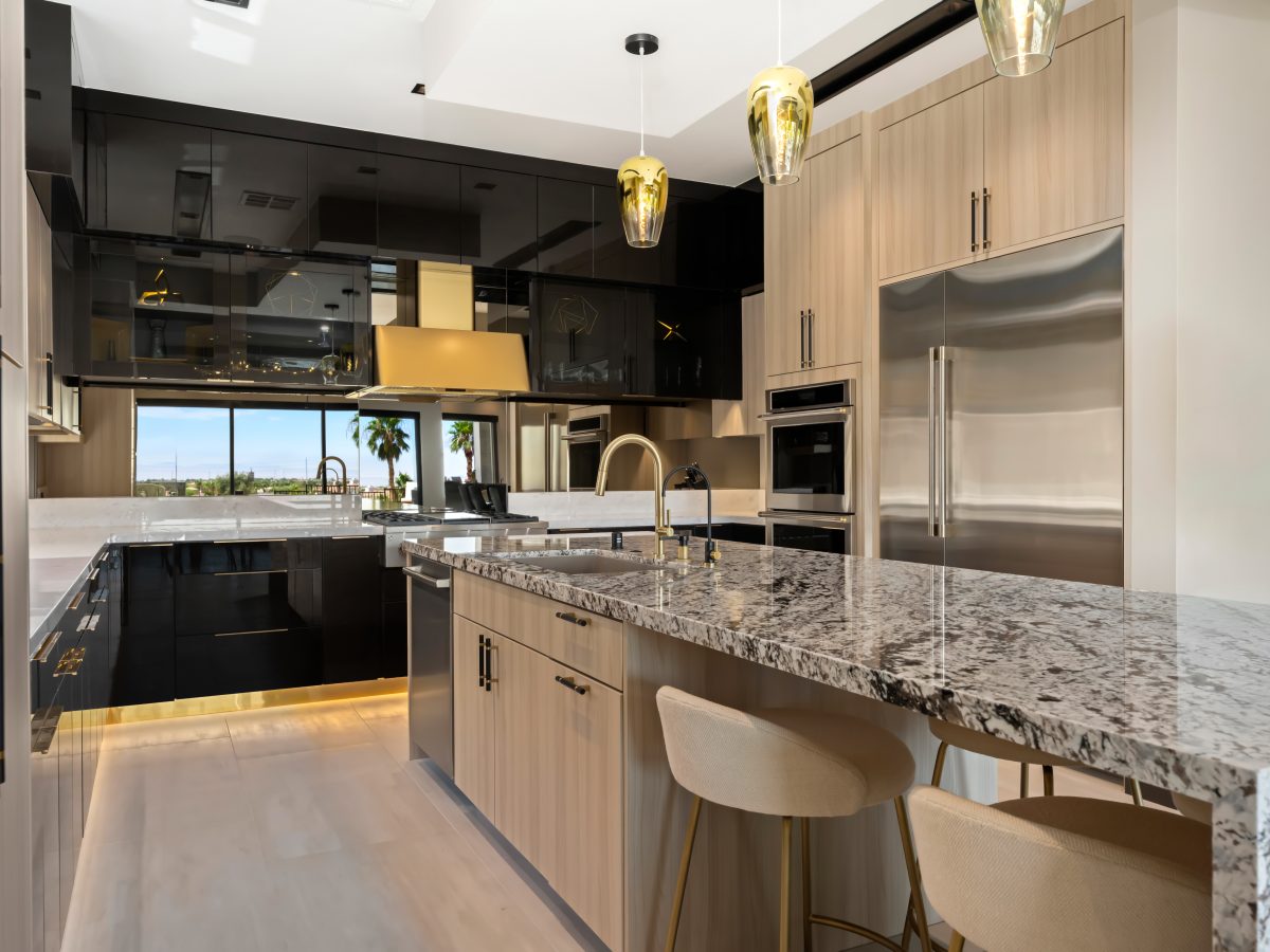 Luxury kitchen with granite island, glossy charcoal cabinetry, and gold range hood — Reveal Interior Design Las Vegas