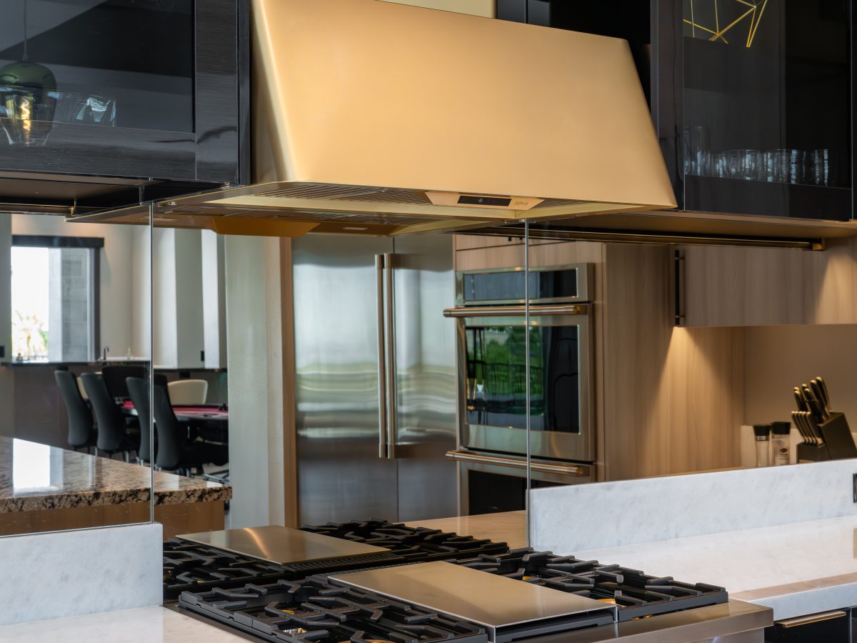Luxury kitchen with gold range hood, mirrored backsplash, and dark charcoal glossy cabinetry — Reveal Interior Design Las Vegas