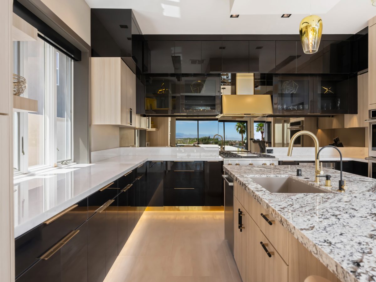 Luxury kitchen with granite island, glossy charcoal cabinetry, and gold fixtures — Reveal Interior Design Las Vegas