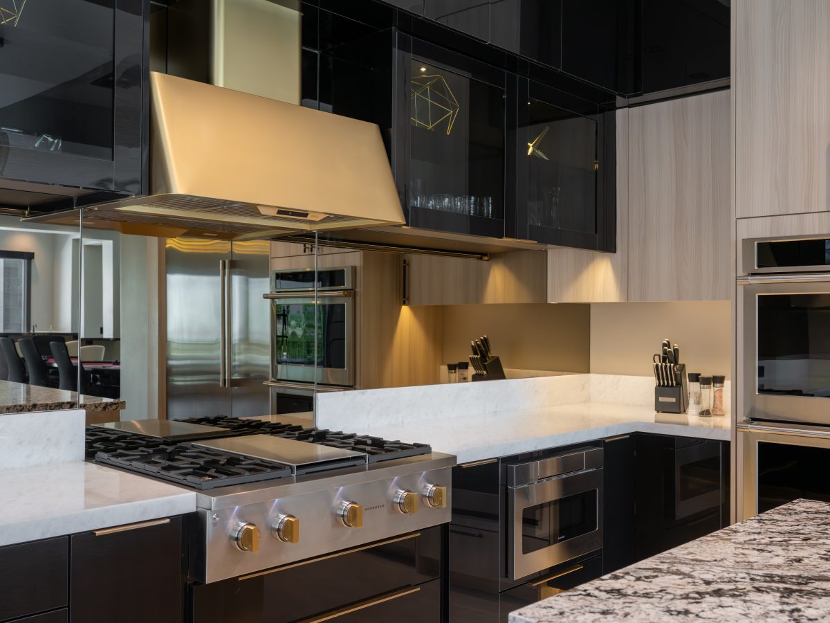 Luxury kitchen with gold range hood, mirrored backsplash, and dark charcoal glossy cabinetry — Reveal Interior Design Las Vegas