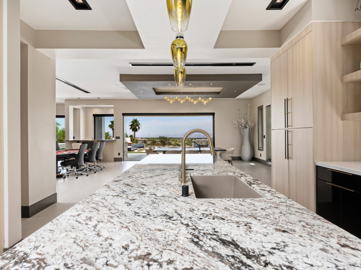 Granite island kitchen with white oak cabinetry, gold fixtures, and mirrored backsplash — Reveal Interior Design Las Vegas