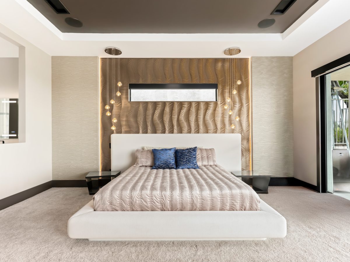 Primary bedroom with gold bronze textured panel accent wall, platform bed, and multi-drop pendant lighting — Reveal Interior Design Las Vegas