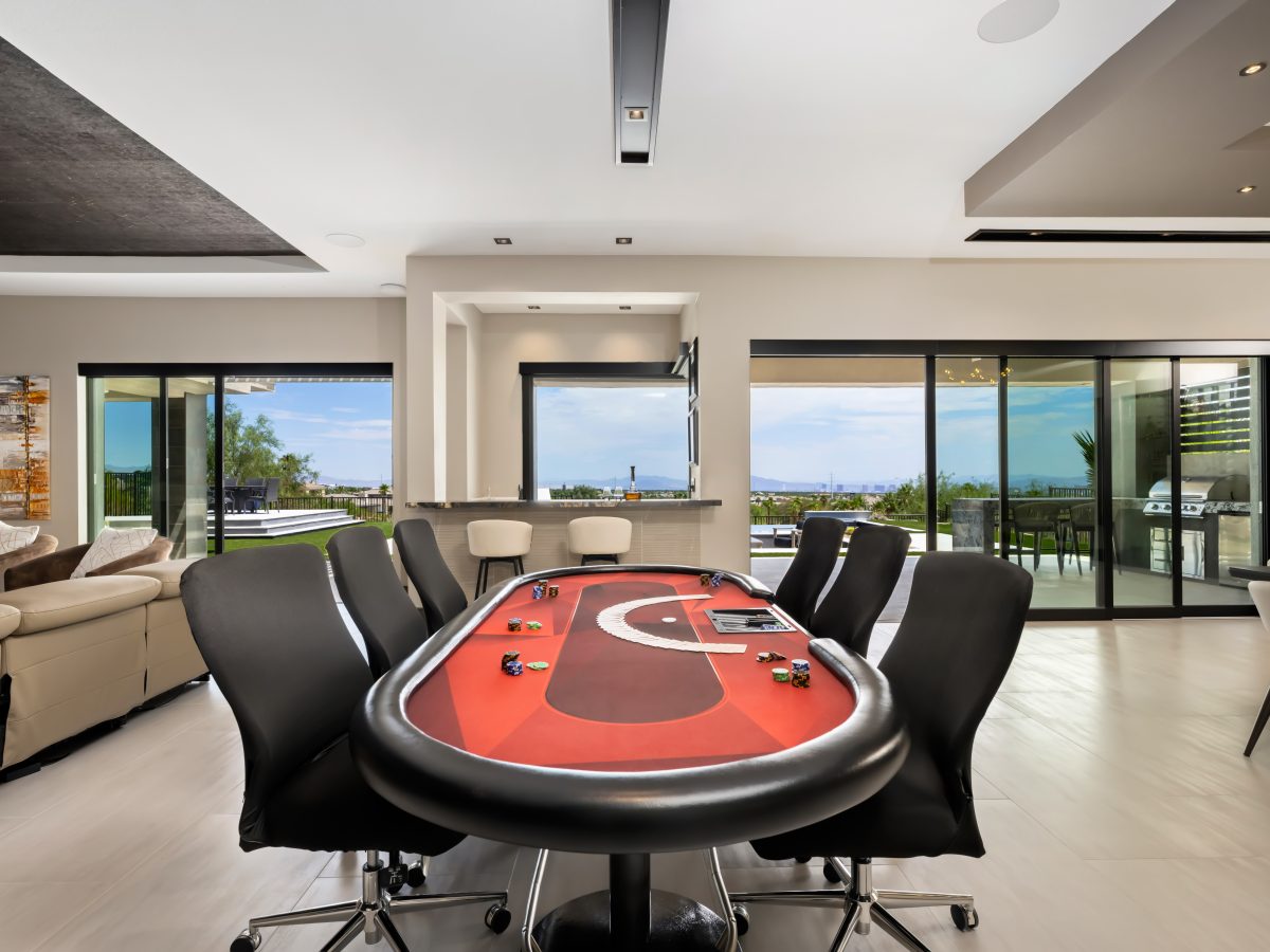 Game room with crimson felt card table and panoramic views — Reveal Interior Design Las Vegas