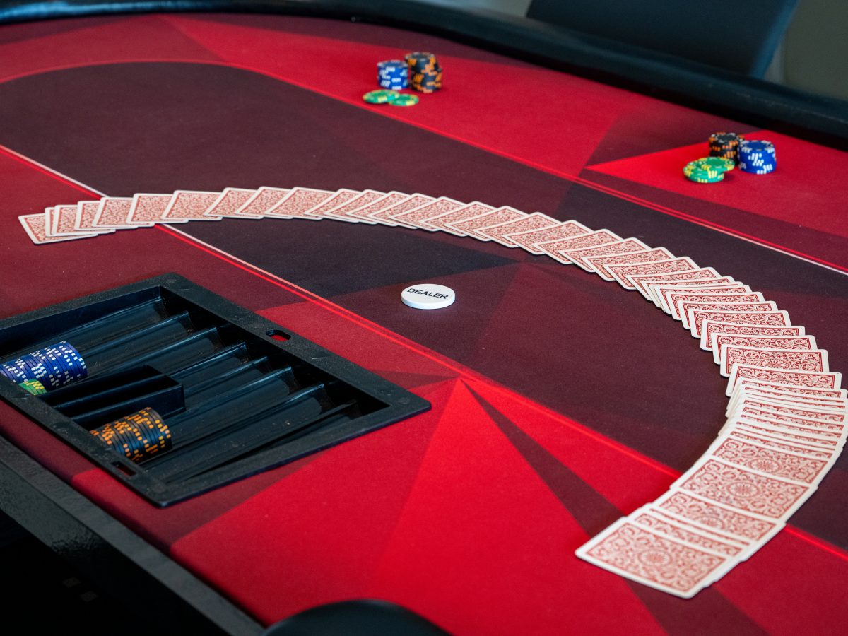 Game room crimson felt card table with dealer chip and spread deck — Reveal Interior Design Las Vegas