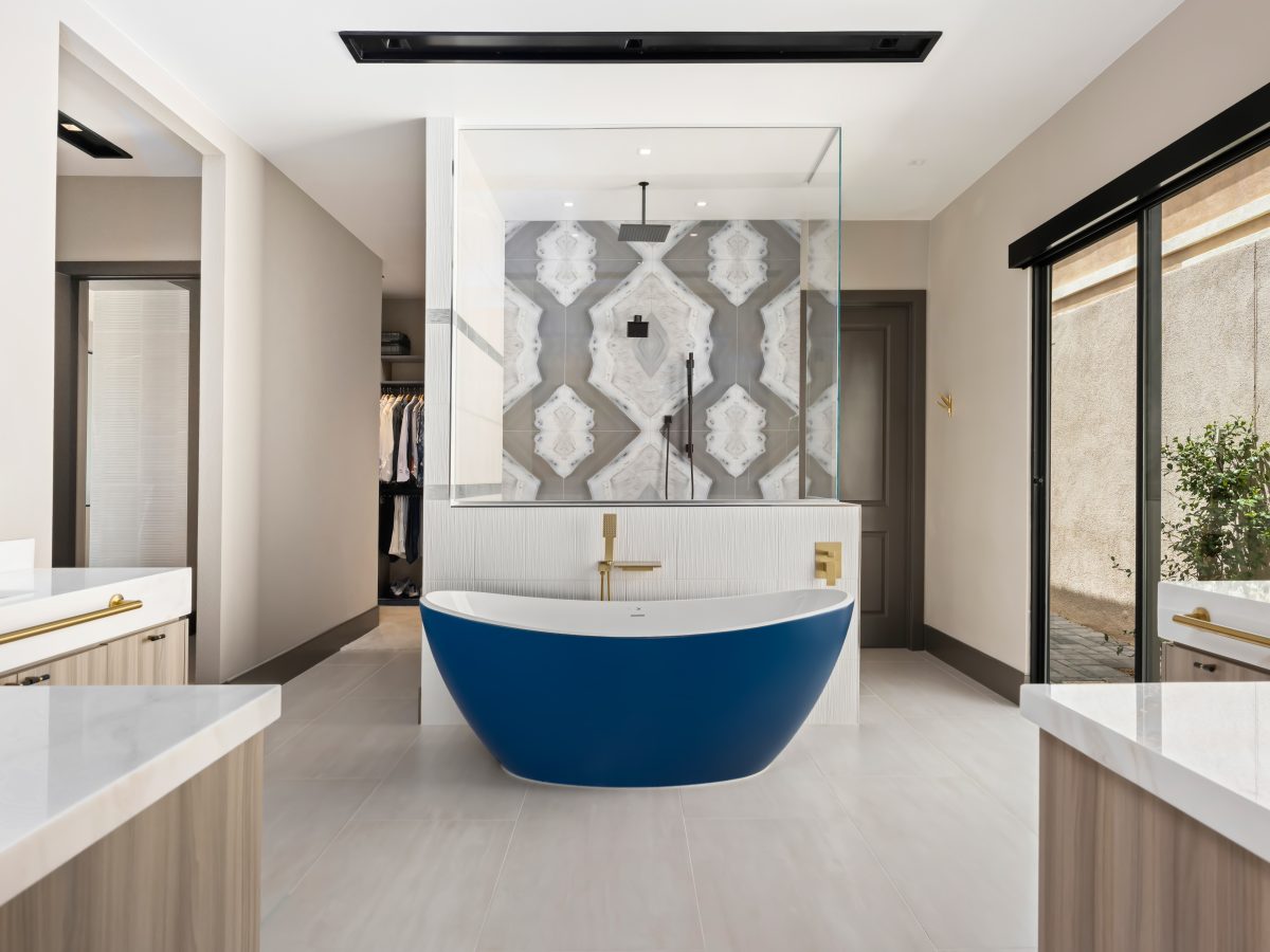 Primary bathroom with cobalt blue freestanding tub, striking porcelain slab shower wall, and gold fixtures — Reveal Interior Design Las Vegas