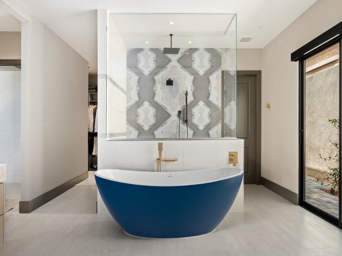 Primary bathroom with cobalt blue freestanding tub, porcelain slab shower wall, and gold fixtures — Reveal Interior Design Las Vegas