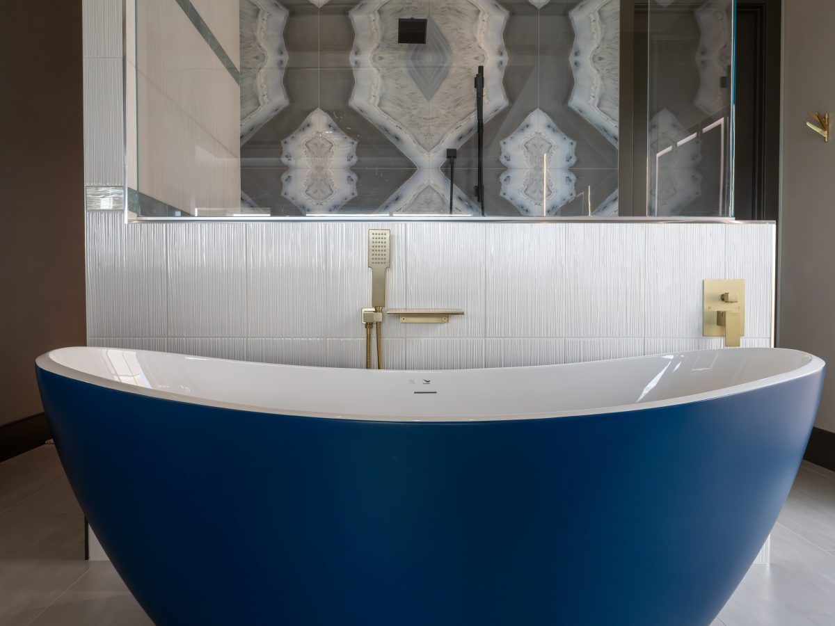 Primary bathroom with cobalt blue freestanding tub, gold fixtures, and porcelain slab shower wall — Reveal Interior Design Las Vegas