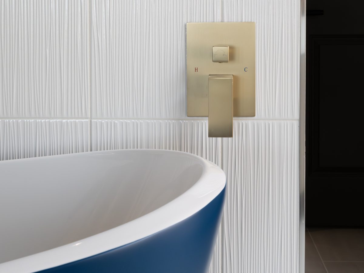 Primary bathroom with cobalt blue freestanding tub, textured white porcelain tile wall, and brushed gold fixtures — Reveal Interior Design Las Vegas