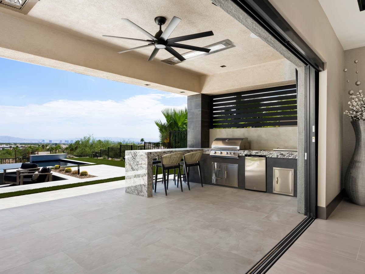 Covered outdoor kitchen with granite island, built-in BBQ, and large-format porcelain tile — Reveal Interior Design Las Vegas
