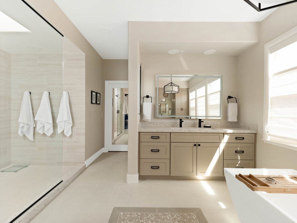 Primary bathroom with warm beige cabinetry, quartz countertops, and freestanding tub — Reveal Interior Design Las Vegas