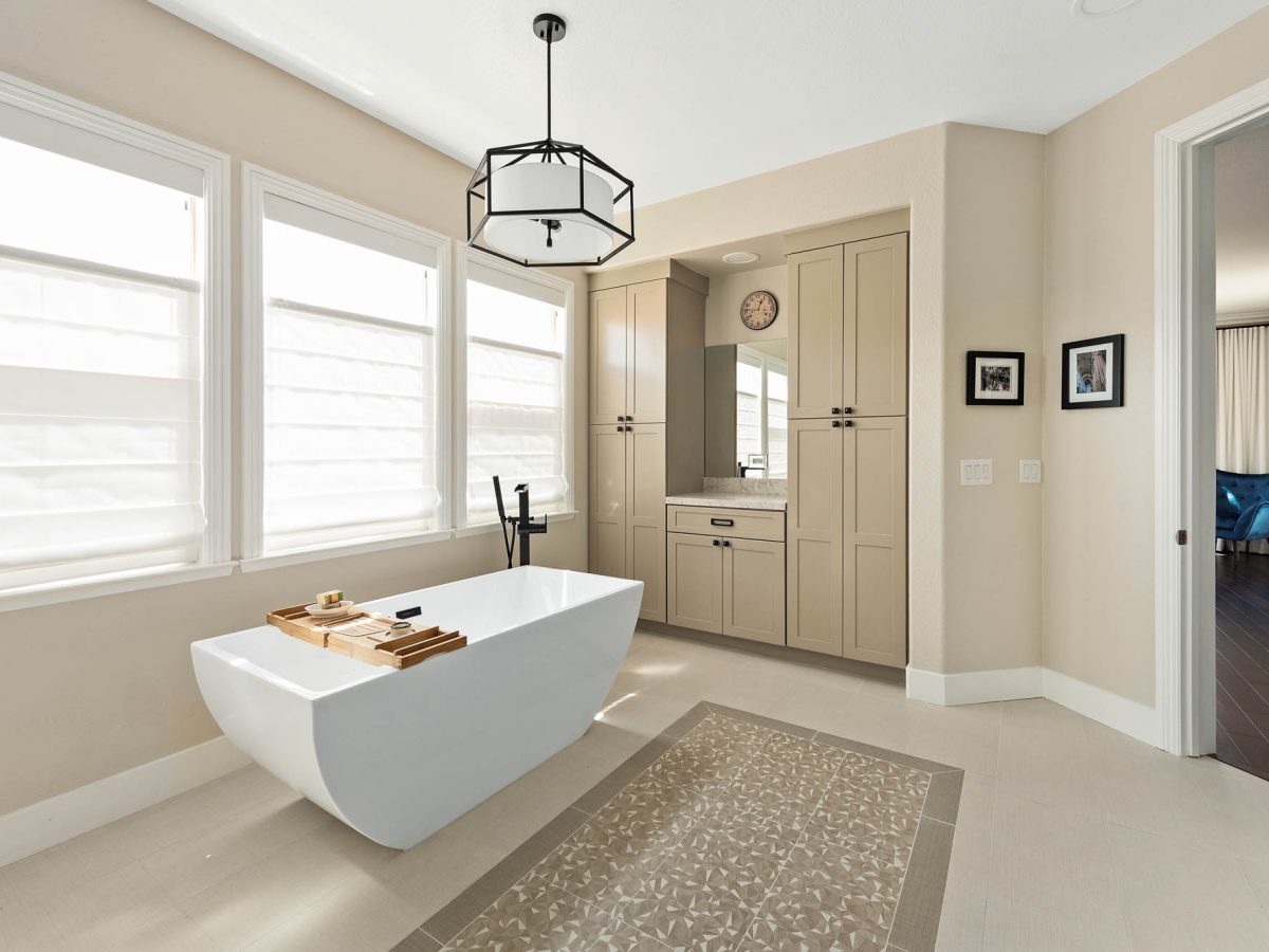 Primary bathroom with freestanding tub, warm beige cabinetry, and quartz countertops — Reveal Interior Design Las Vegas