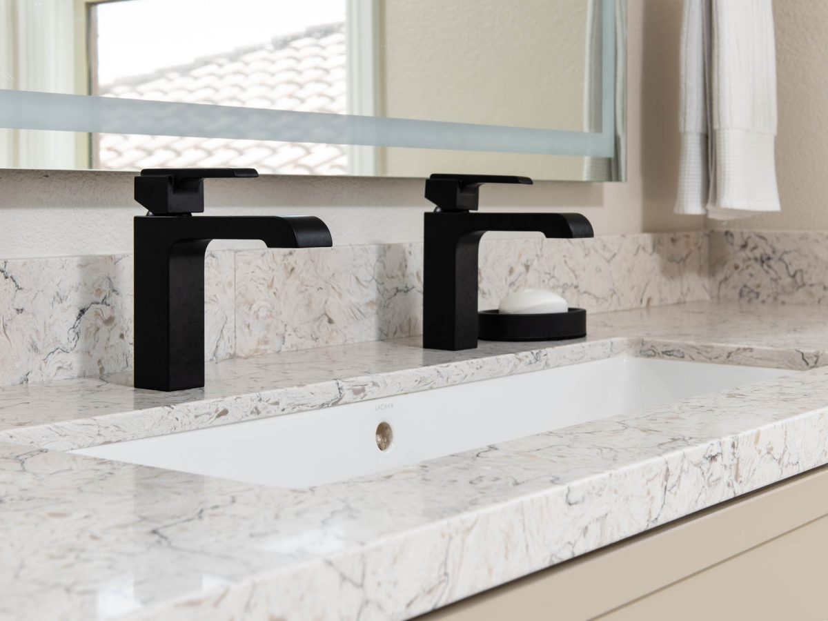 Primary bathroom trough sink with white and beige veined quartz countertop and dual black single-hole faucets — Reveal Interior Design Las Vegas