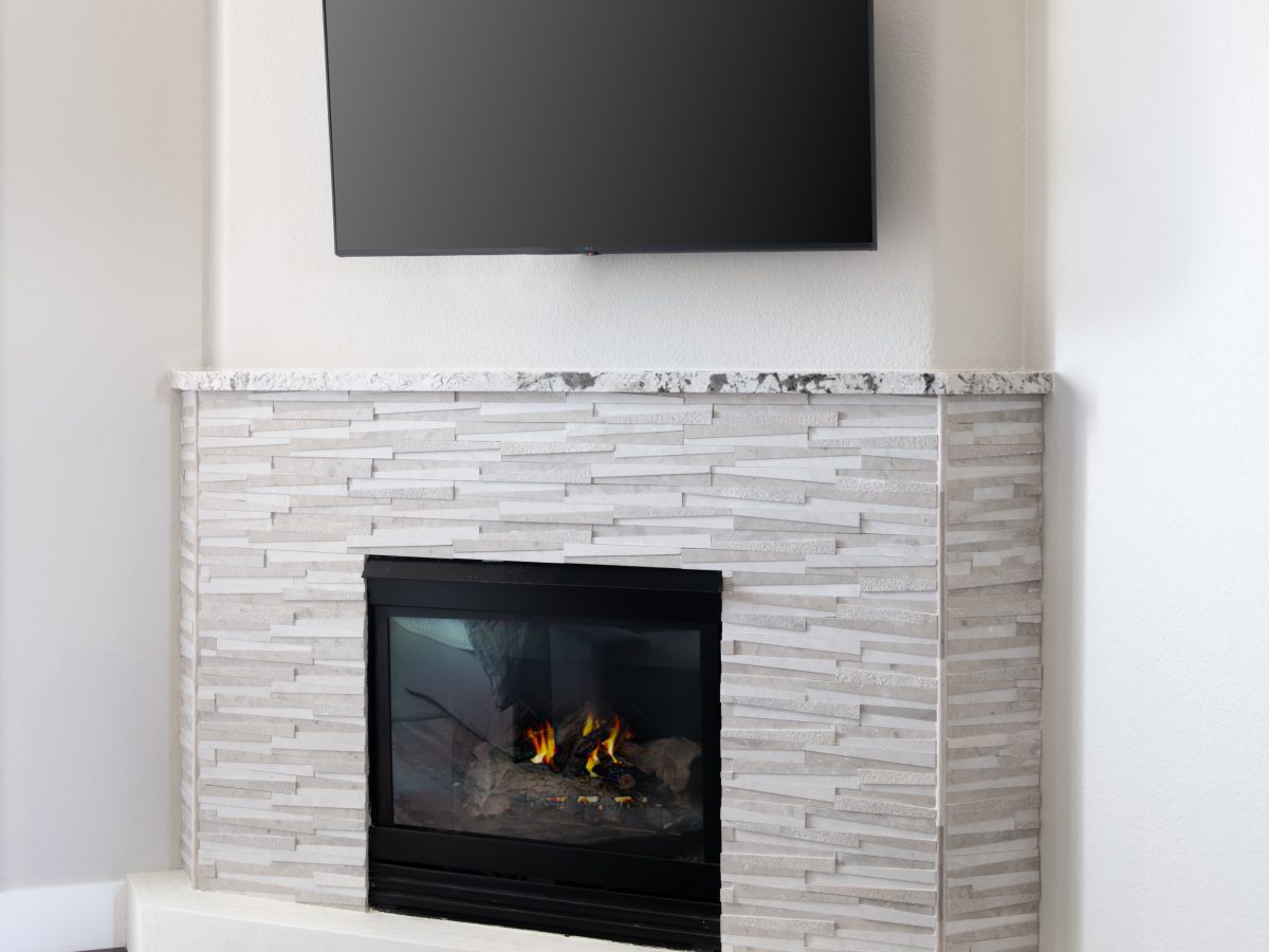 Corner fireplace with dimensional stone surround and granite mantel — Reveal Interior Design Las Vegas