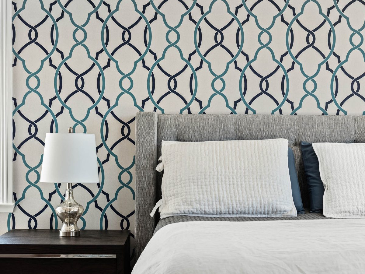 Primary bedroom with teal and navy geometric wallpaper accent wall and gray upholstered king bed — Reveal Interior Design Las Vegas