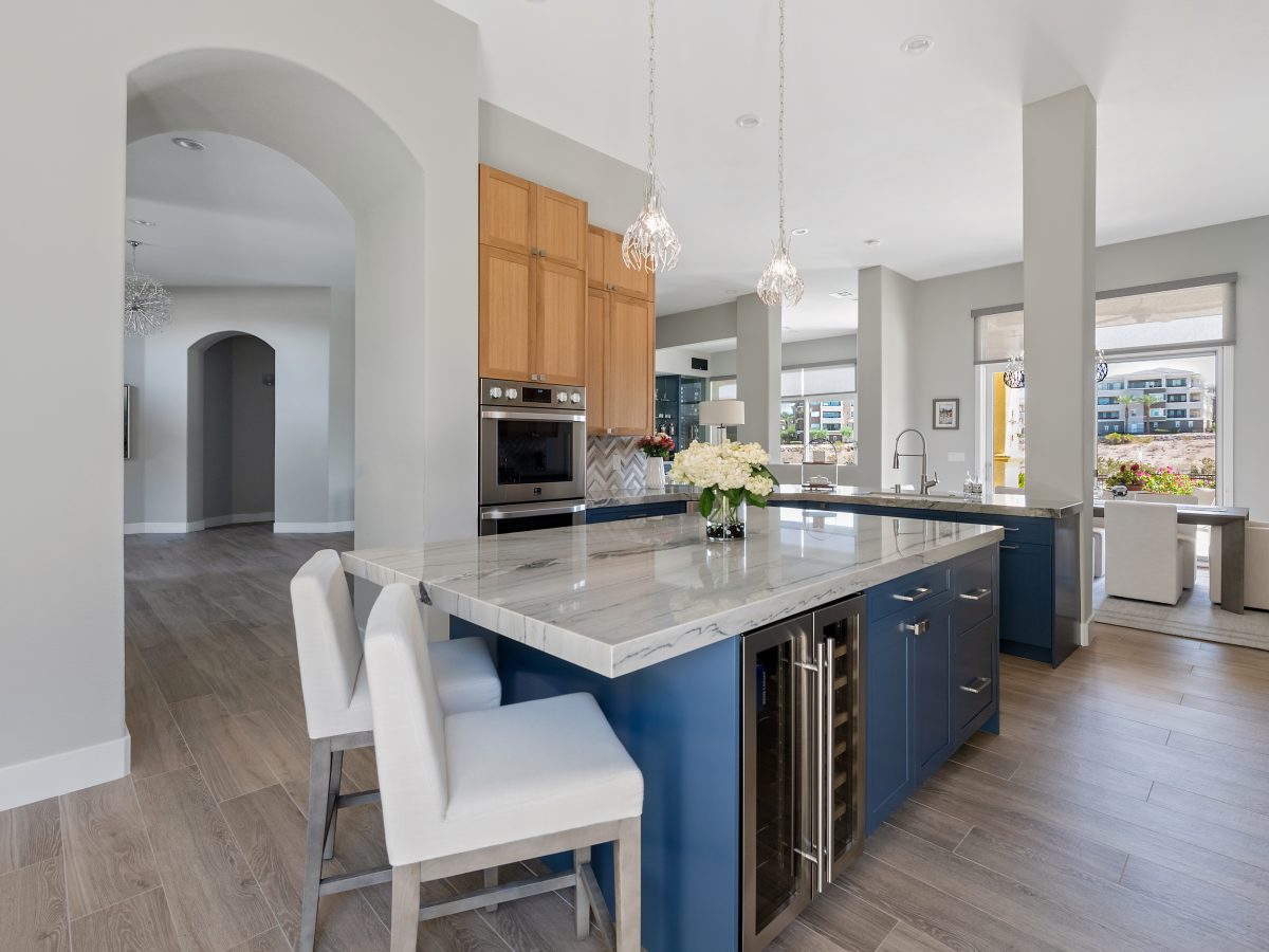 Kitchen with dark navy island, warm oak upper cabinets, and quartzite countertops — Reveal Interior Design Las Vegas