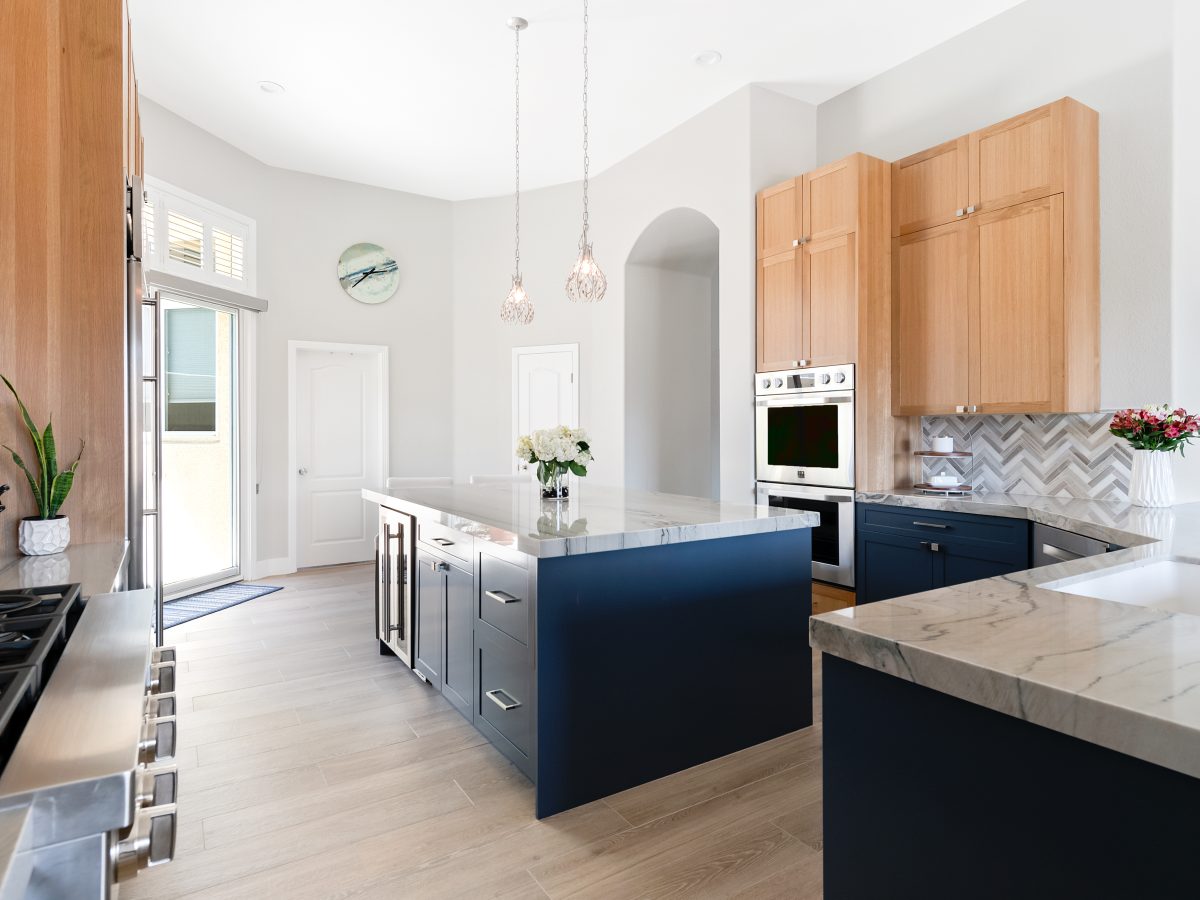 Kitchen with navy blue base cabinets, warm oak uppers, and quartzite countertops — Reveal Interior Design Las Vegas