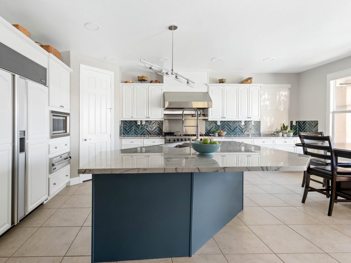Kitchen with blue-veined quartzite island, teal herringbone backsplash, and white cabinetry — Reveal Interior Design Las Vegas