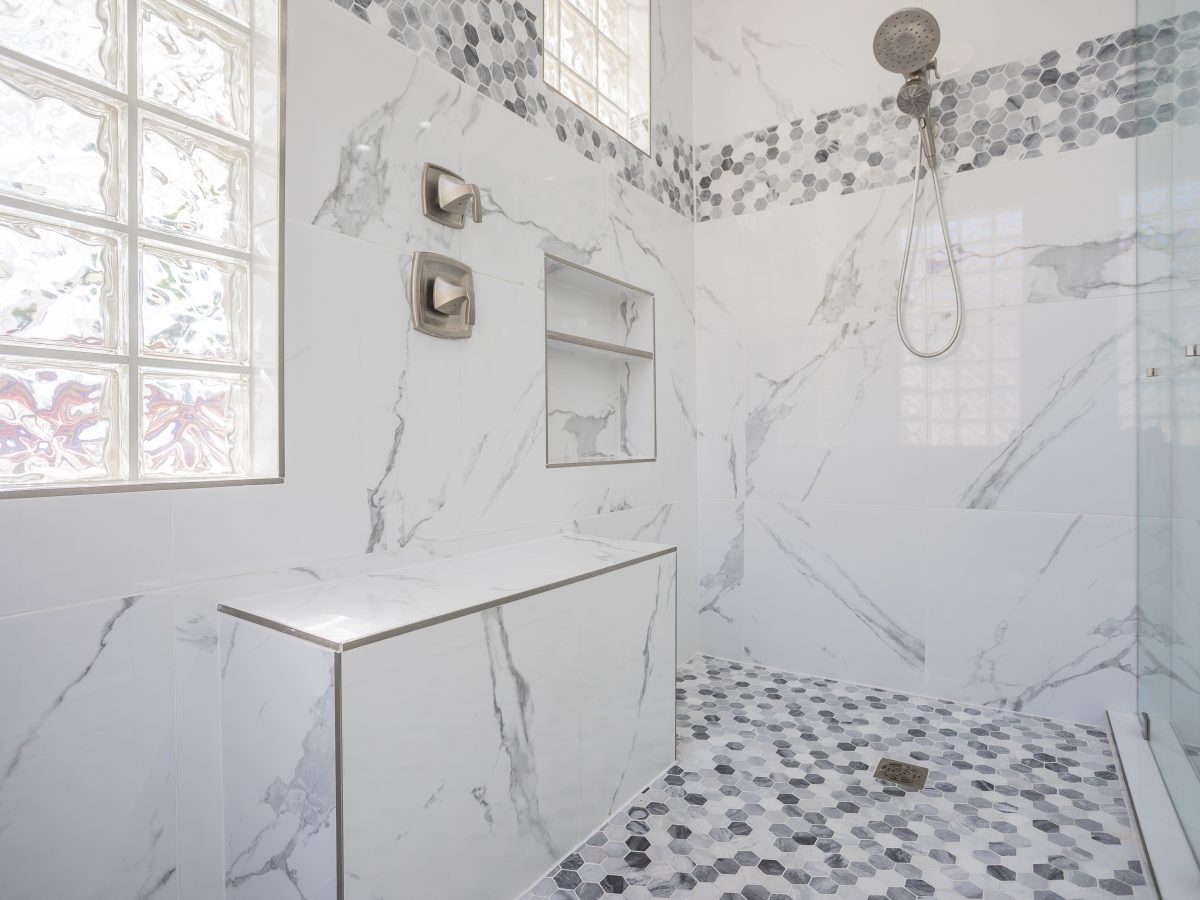 Primary bathroom with marble-look porcelain shower walls and geometric mosaic tile accents — Reveal Interior Design Las Vegas