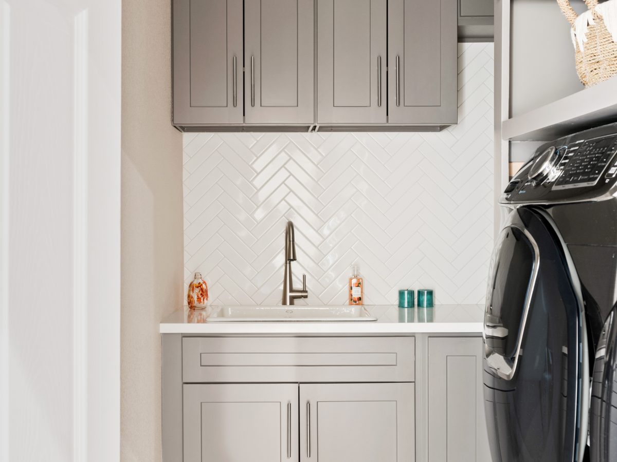 Laundry room with taupe shaker cabinets, herringbone subway tile backsplash, and encaustic floor tile — Reveal Interior Design Las Vegas