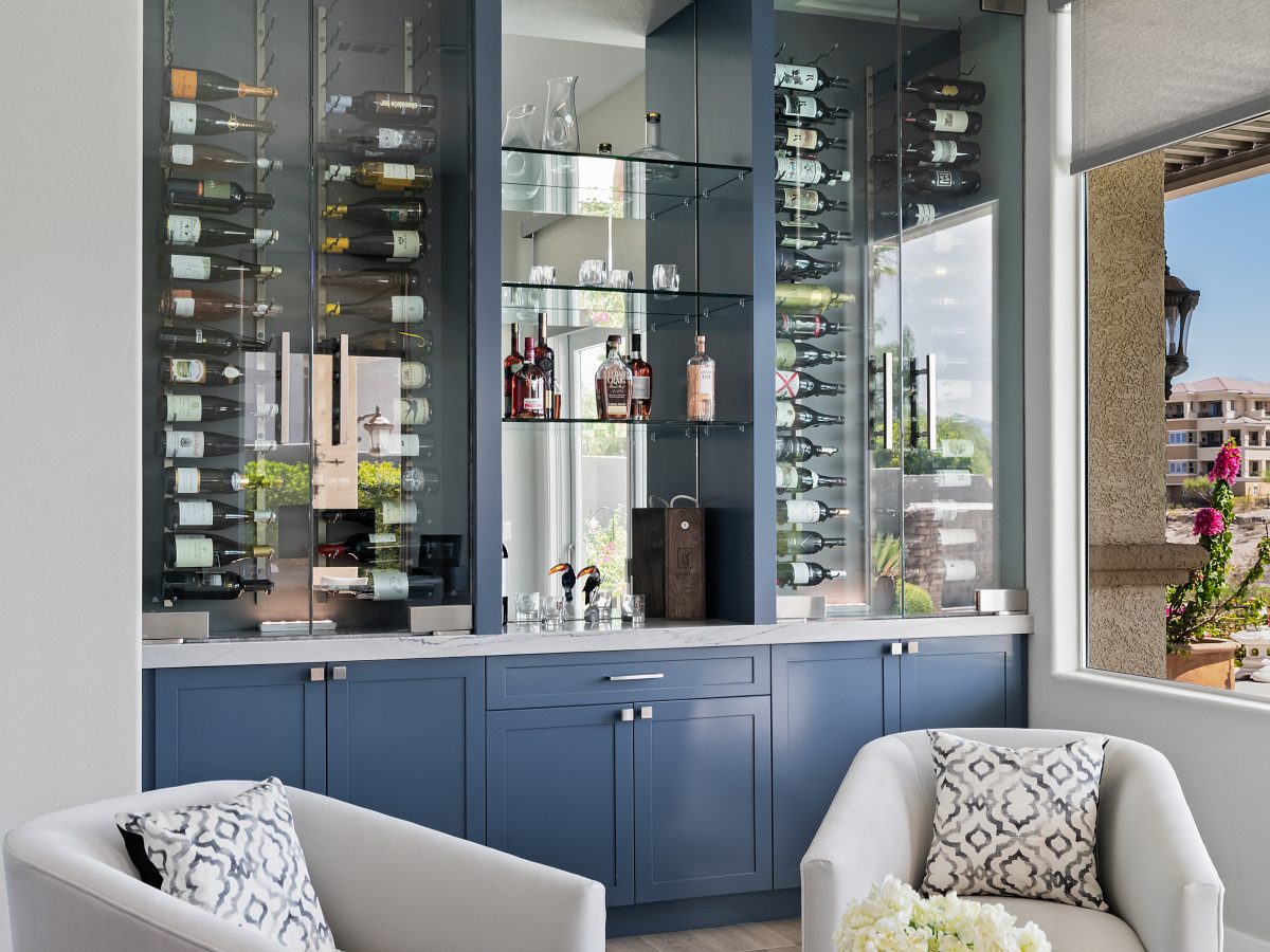 Lounge bar with blue cabinetry, glass-enclosed dual-zone wine coolers, and mirrored shelving — Reveal Interior Design Las Vegas