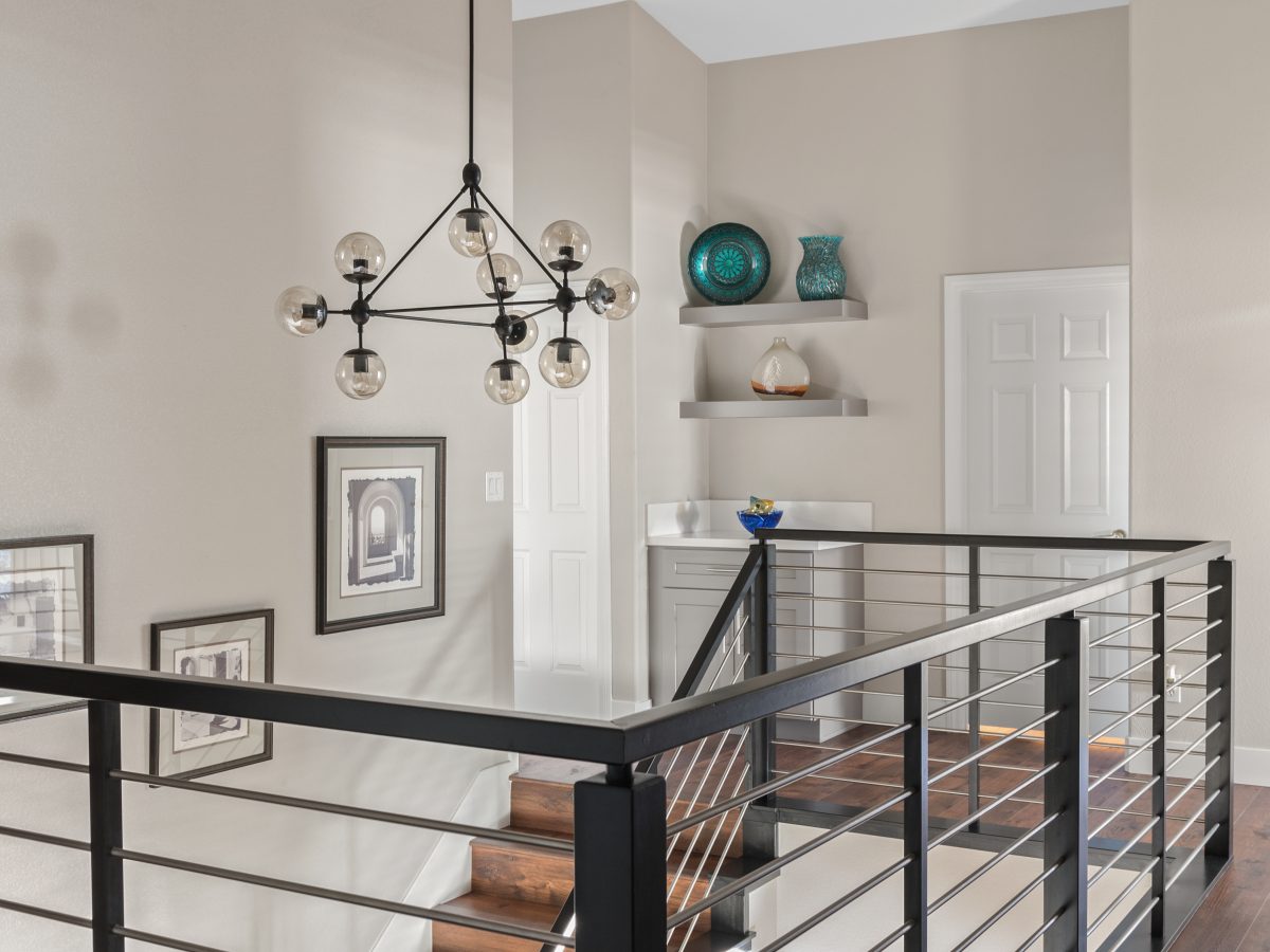 Upstairs hallway with sputnik chandelier, black metal stair railing, and floating shelves — Reveal Interior Design Las Vegas