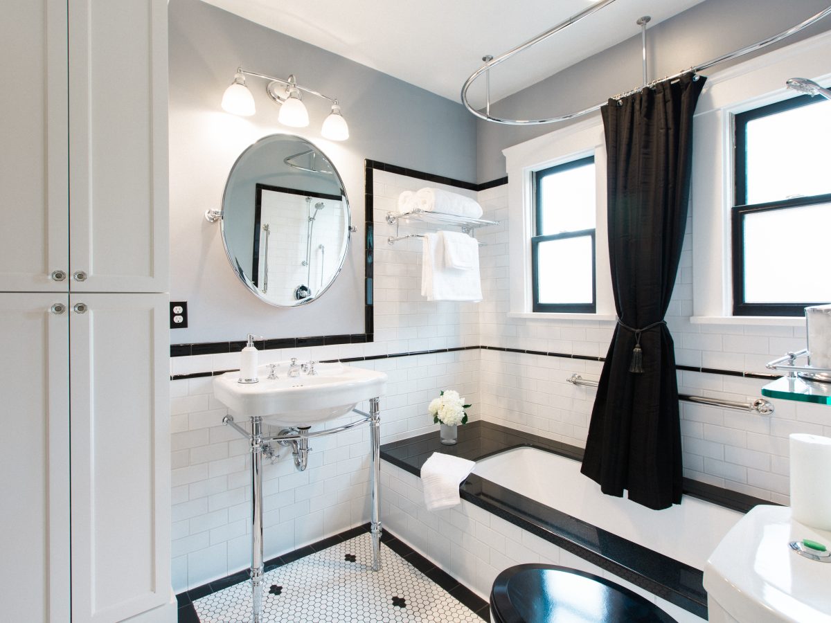 1920s-style black and white bathroom with hex mosaic floor, subway tile, and black granite tub surround — Reveal Interior Design Las Vegas