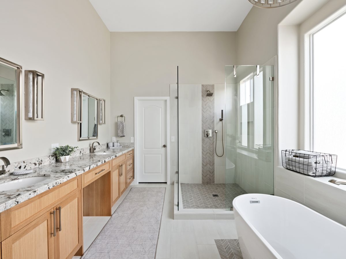 Primary bathroom with warm oak vanity, granite countertops, and glass-enclosed shower — Reveal Interior Design Las Vegas
