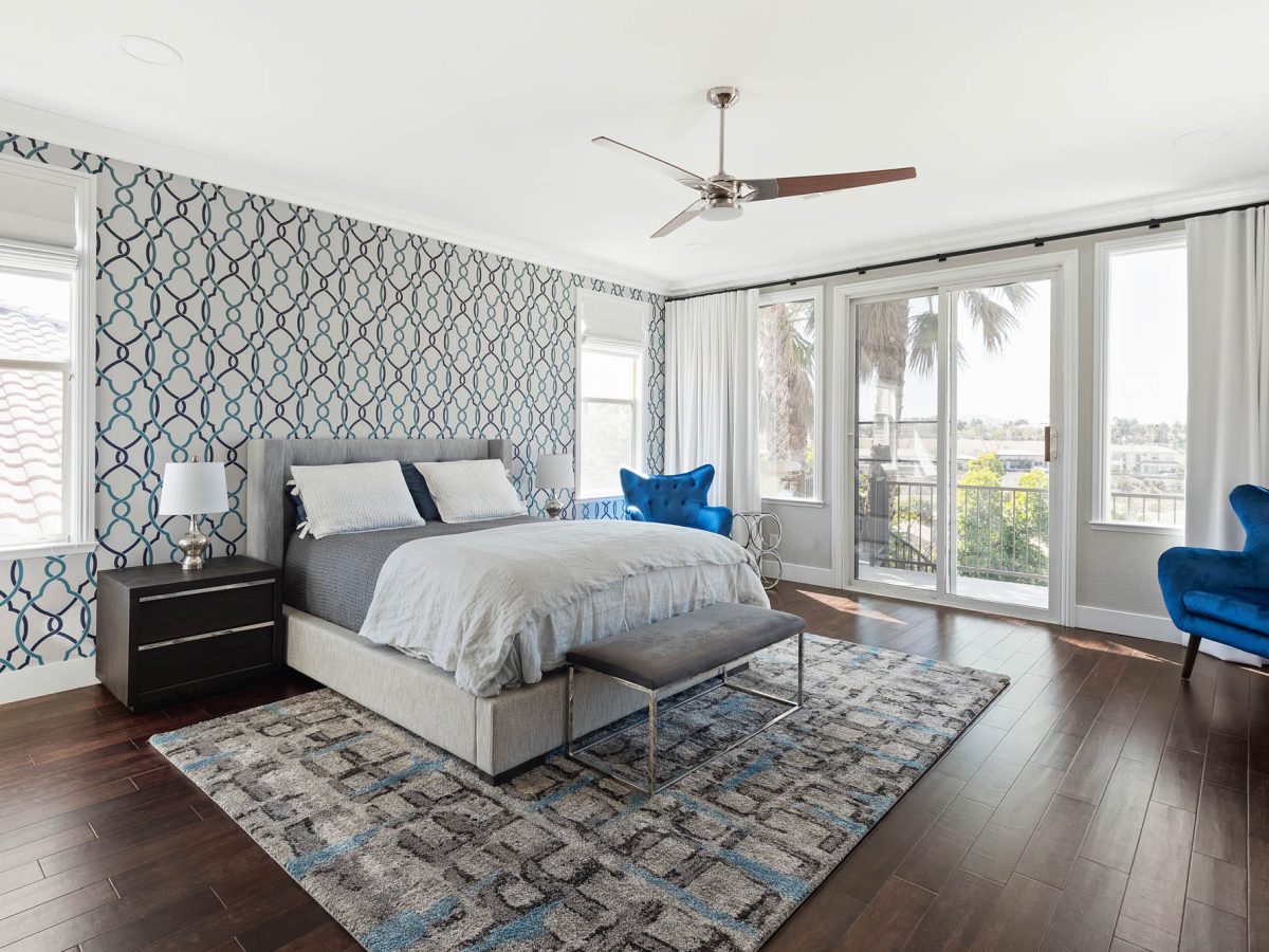 Primary bedroom with teal and navy geometric wallpaper accent wall and gray upholstered king bed — Reveal Interior Design Las Vegas