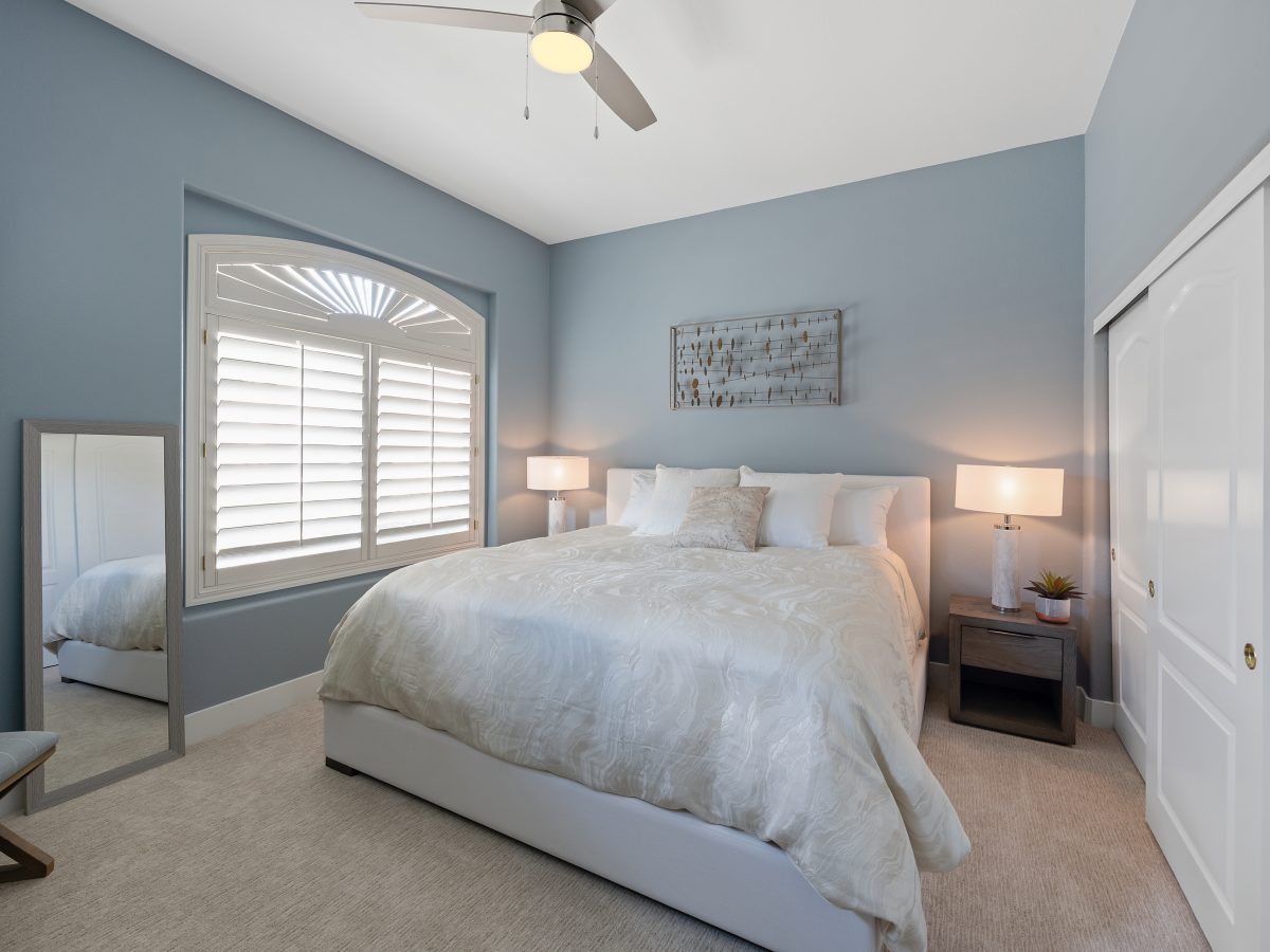 Primary bedroom with slate blue accent wall and tall upholstered headboard — Reveal Interior Design Las Vegas