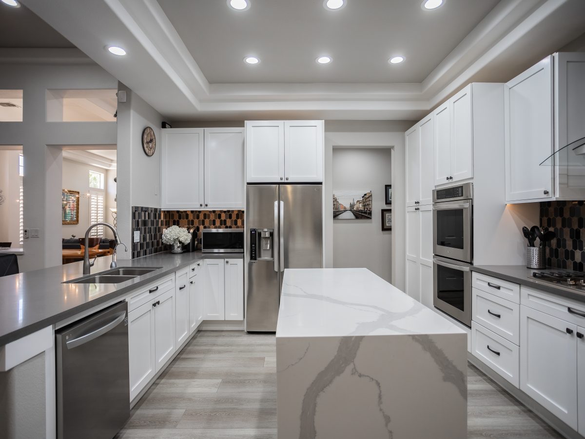 White shaker kitchen with statuario-style quartz waterfall island and hex mosaic tile backsplash — Reveal Interior Design Las Vegas