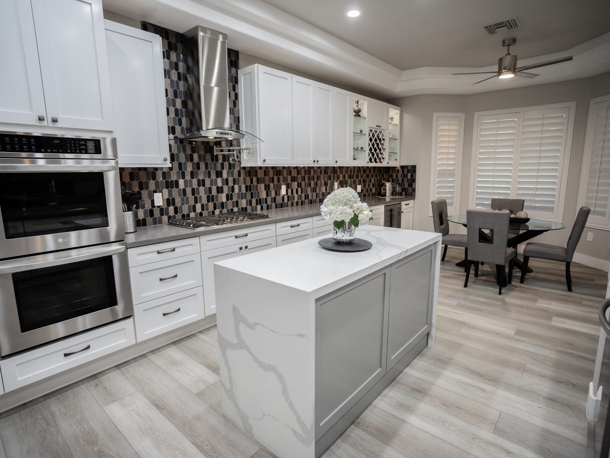 White shaker kitchen with statuario-style quartz waterfall island and hex mosaic backsplash — Reveal Interior Design Las Vegas
