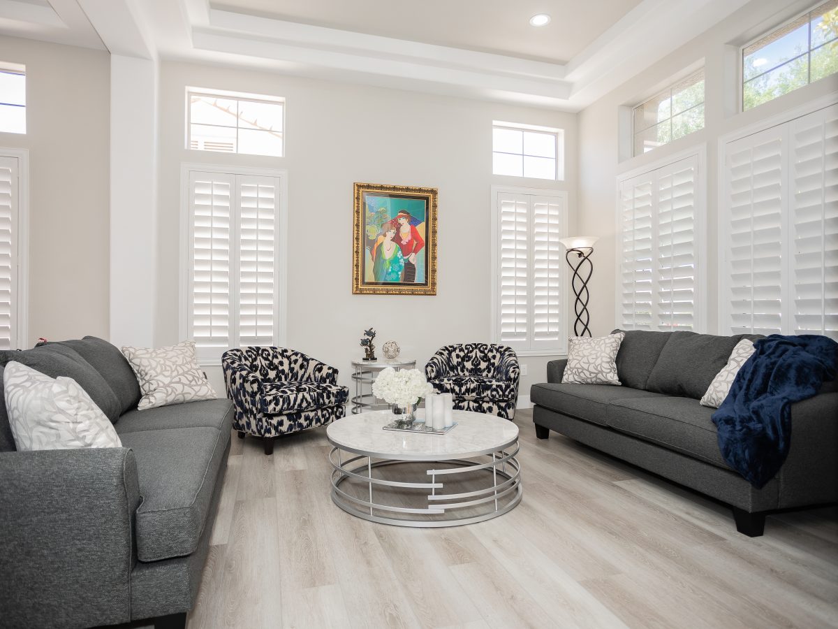 Living room with gray sofas, stone-look round coffee table, and patterned accent chairs — Reveal Interior Design Las Vegas