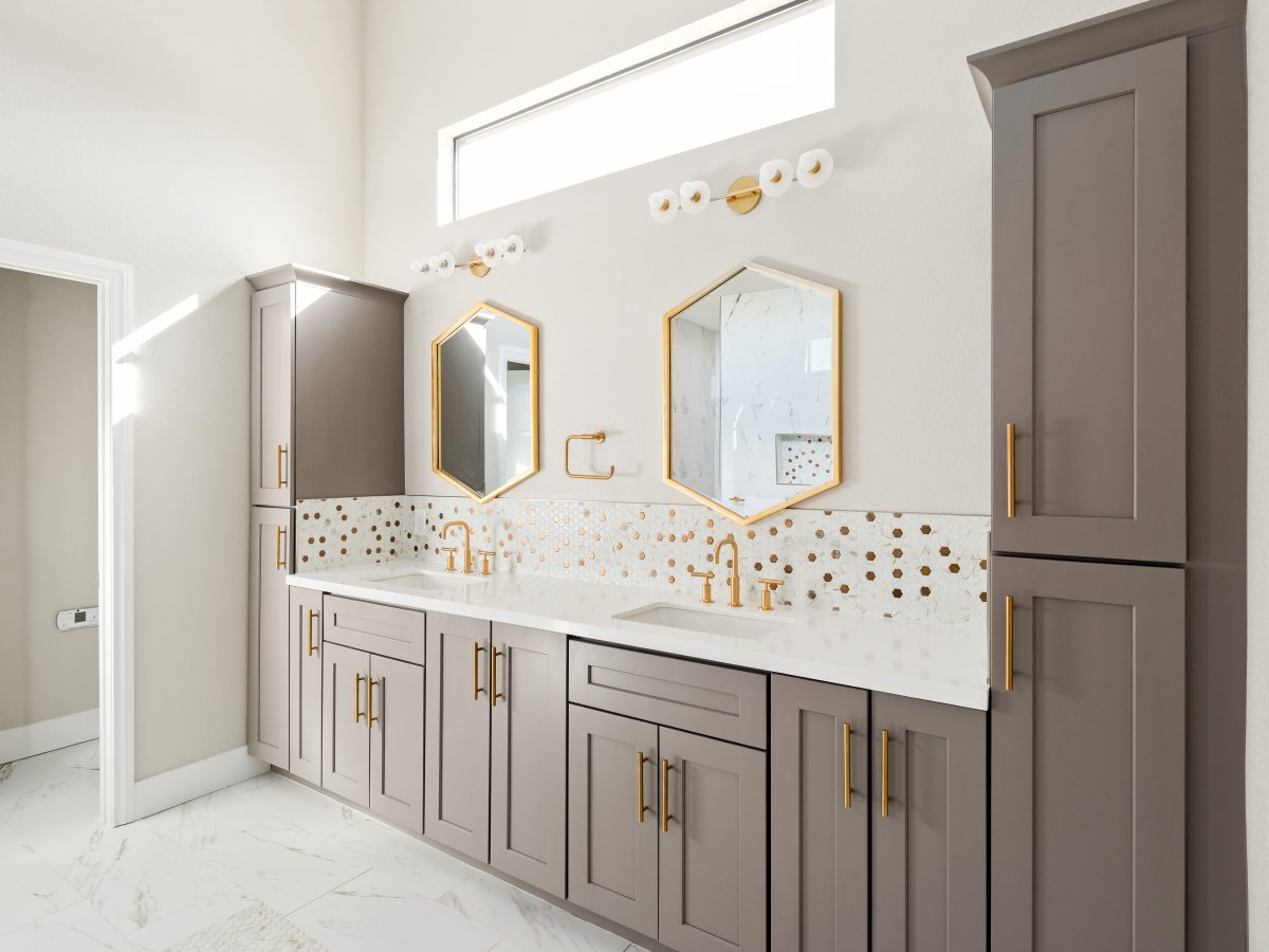 Primary bathroom with taupe shaker cabinetry, gold mosaic tile backsplash, and geometric mirrors — Reveal Interior Design Las Vegas