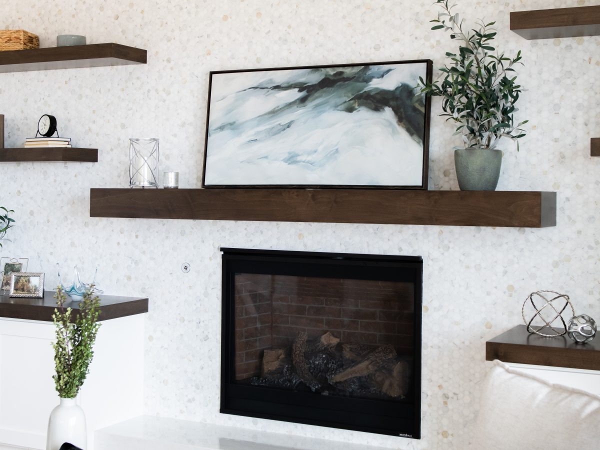 Family room fireplace wall with dark-stained wood mantel, floating shelves, and geometric marble tile — Reveal Interior Design Las Vegas